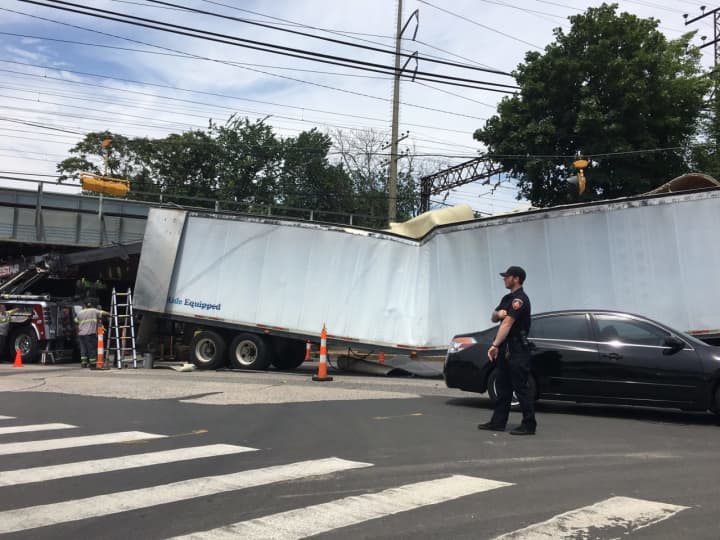 A Stamford police officer directs traffic around a wrecked tractor-trailer that tried and failed to negotiate a railroad underpass on East Main Street in Stamford.