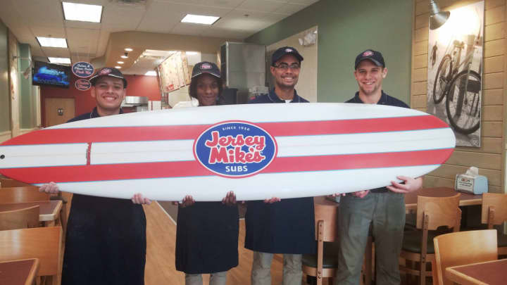 The staff of Jersey Mike&#x27;s in East Rutherford proudly show off the surfboard that hangs in the shop as a  reminder of its Jersey shore origins.