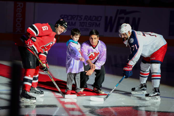 Devils Capt. Andy Greene and Blue Jackets Capt. Nick Foligno are joined by 7-year-old Quinn Knapp of Cranford and 17-year old Alex Walsh of Fair Lawn for a ceremonial puck drop at the home team’s Hockey Fights Cancer night.