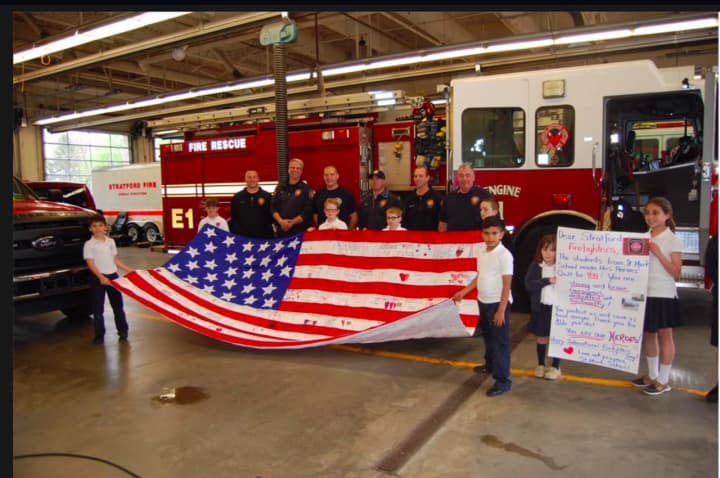 Members of “A” Platoon Headquarters Companies of the Stratford Fire Department, along with students from St Mark Elementary School, displaying the flag at Stratford fire department headquarters.