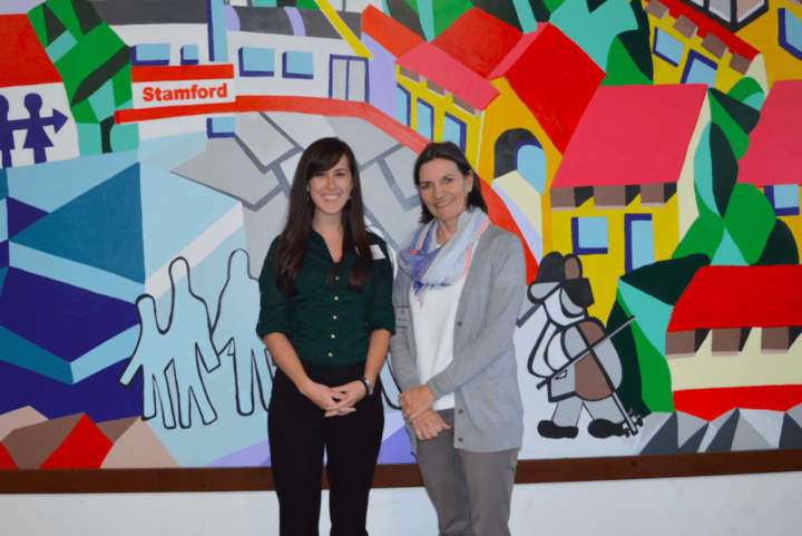 From left, Christa Chu, development and communications manager; and Catalina Horak, executive director of Neighbors Link Stamford.  They are standing in front of a mural created by a Mexican immigrant with help from over 200 volunteers.