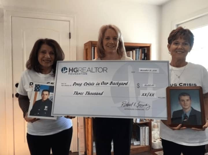 Carol Christiansen, left, and Susan Salomone, co-founders of Drug Crisis in Our Backyard, hold photos of the sons they lost to drug addiction. Lin Crispinelli of Hudson Gateway Association of REALTORS®, displays a facsimile of the $3,000 check.