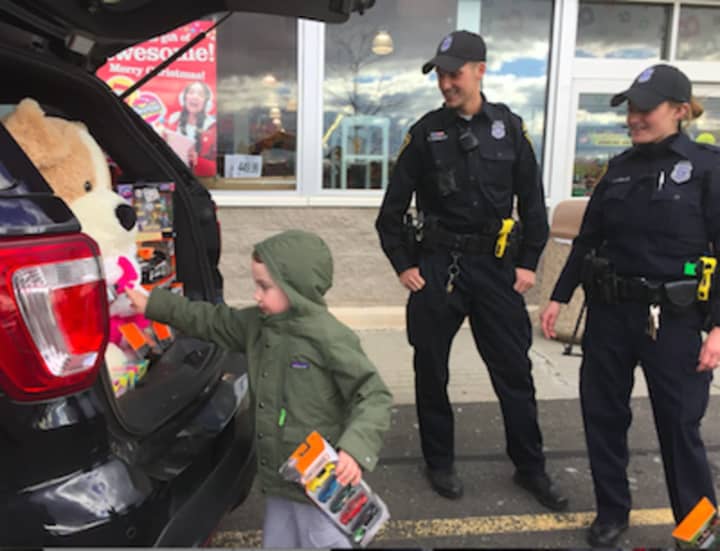 Eamon Gorman, 4, from Norwalk, contributes toys during the Norwalk Police Department&#x27;s Stuff A Cruiser event at Toys &#x27;R Us. Looking on are officers Keith Torreso and Sara Laudano.