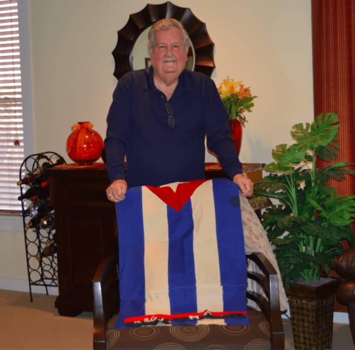 Cuban native Celestino Heres in his Norwalk home.  He is holding the Cuban flag that his late mother made at the end of the Cuban Revolution.