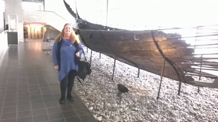 Lydia Higginson stands next to Viking ship at a Viking museum.