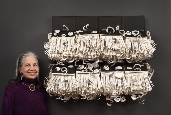 Irmari Nacht of Englewood and her large recycled bookwork — composed of 8 identical books cut into swirls, spirals, and strips.