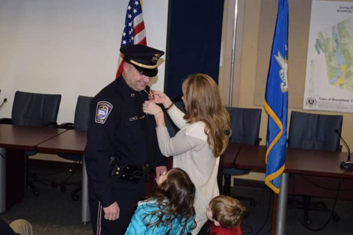Maryann Frengs, the wife of Brookfield Police Department Pete Frengs, pins on his Captain&#x27;s badge as their children watch at the ceremony.