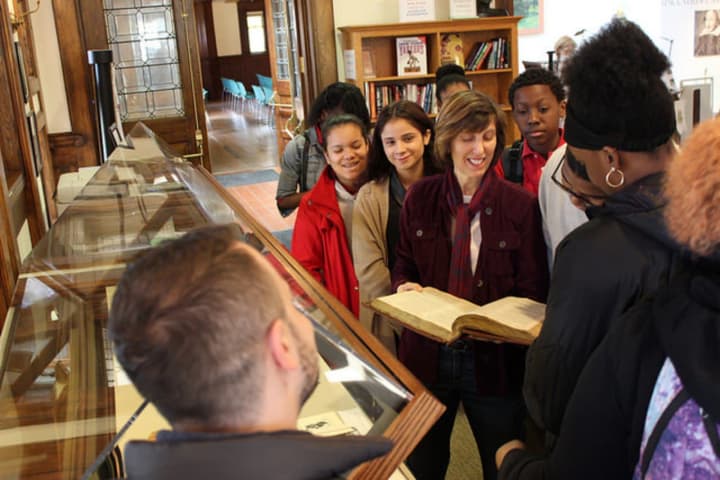 Volunteer docent Lynne Van Winkle shows a rare book from the Pequot Library&#x27;s Special Collections to students in the reading room.