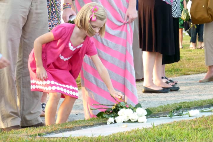<p>A child places a white rose on the 9/11 Memorial at Sherwood Island State Park in Westport at a past ceremony.</p>