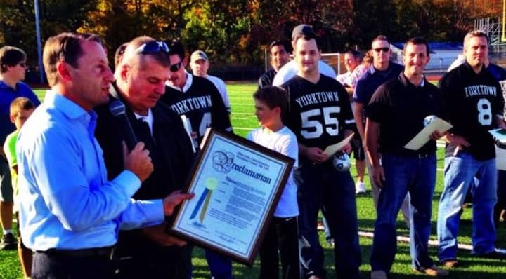 Surrounded by former players, Ron Santavicca accepts a certificate declaring Saturday, Oct. 5 as Ron Santavicca Day in Westchester from County Executive Rob Astorino in a ceremony honoring the 1993-94 state title teams at halftime Saturday, Oct. 5.
