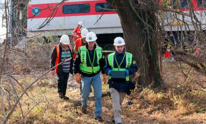 NTSB officials retrieve an event recorder from the derailed Metro-North train in the Bronx, N.Y. The train car behind them has the red stripe and seal of Connecticut on it. 