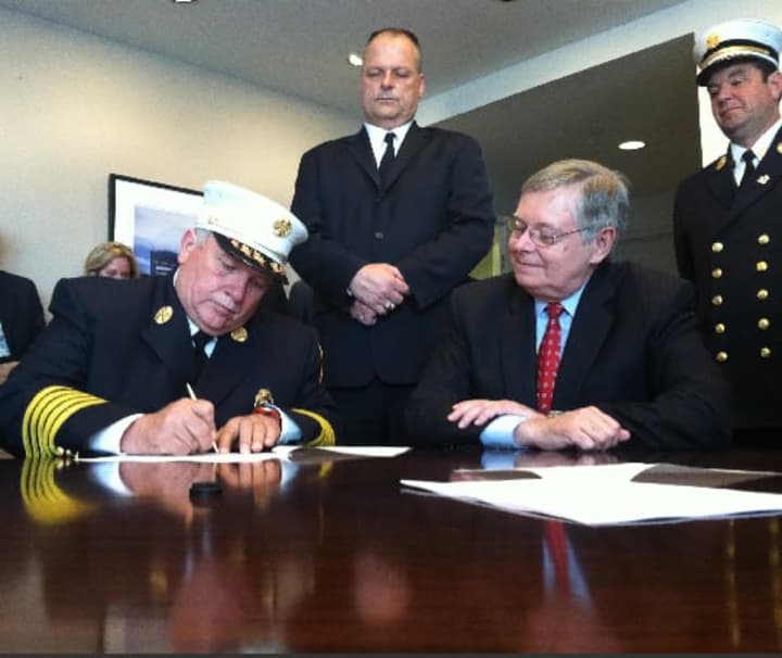 Stamford Fire Department Chief Peter Brown signs an agreement consolidating services with Turn of River Volunteer Fire Department as Stamford Mayor David Martin, sitting, looks on. 