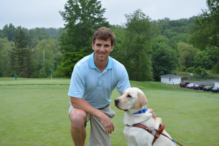 Eli Manning poses for photos with Jansen, a male yellow Labrador who is a guide dog in training.