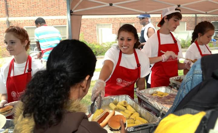Students in the annual Community Connections service immersion program at Sacred Heart University serve dinner at the Feel the Warmth community BBQ in Bridgeport.