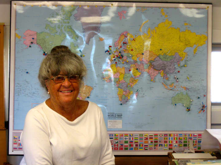 Pat Atkin of Atkin &amp; Co. sits in front of the world map marked with locations that have received wooden boat plans from her 108 -year-old Darien business. 