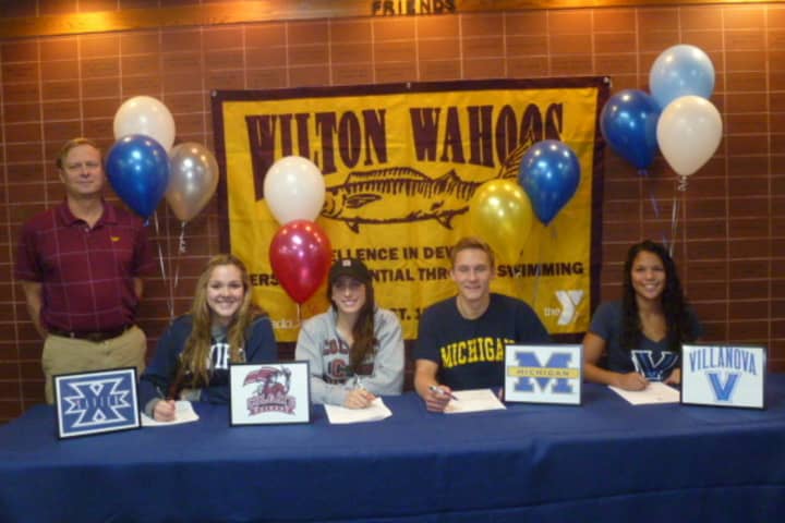 Swimmers for the Wilton Wahoos, from left, Maggie Kauffeld, Courtney Gilroy, Stephen Holmquist and Samantha Cheruk sign letters of intent to college programs. Randy Erlenbach, the team&#x27;s Director of Aquatics, watches them sign the letters.