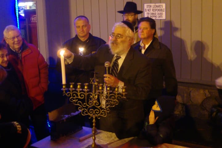 Rabbi Yehoshua Hecht of Beth Israel of Westport/Norwalk lights candles on the menorah, assisted by Chief Thomas Kulhawik and Stew Leonard Jr.