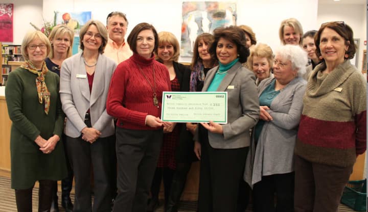 Cathy Pierce of Wilton Social Services accepts a donation check from Wilton Library executive director Elaine Tai-Lauria as members of the library staff look on.