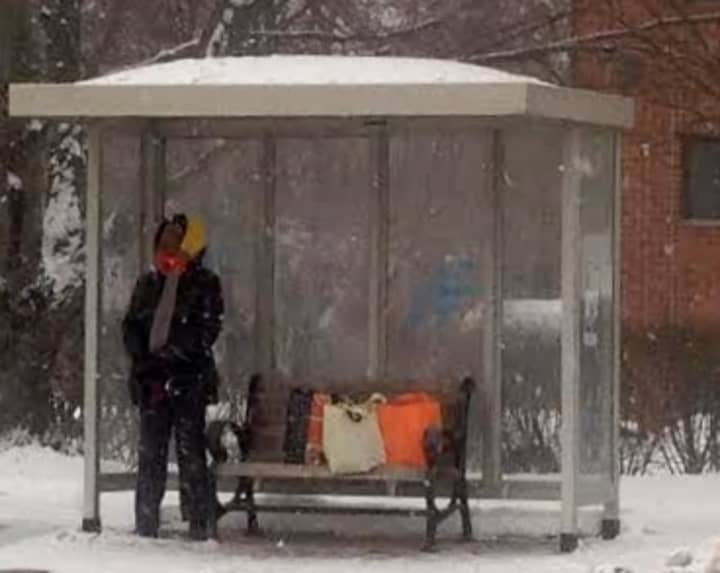 A woman waits at a bus stop on Main Street in Danbury late Monday afternoon as snow falls. 
