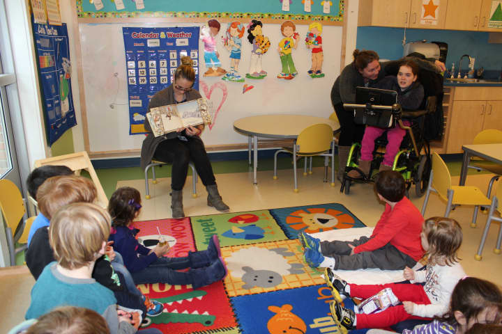 DHS student Lauren Stevens (far right) reading a book to HPNS students with the help of her computerized device and aide Piper Garner (second from right) and teacher Brittany Wainacht (holding book on far left).&quot; 