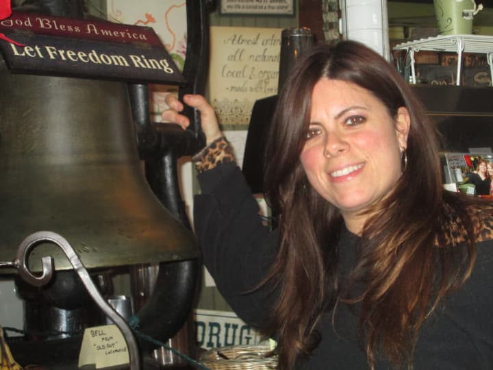 Donna Massaro standing in front of a historic bell that was used for the Old Putnam Line at the Freight House Cafe.