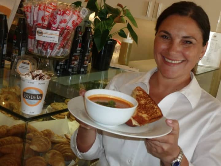 Faina Yelensky, owner of Café Oo La La in Stamford holds up a hot soup and a hot sandwich while hot drink rests nearby.