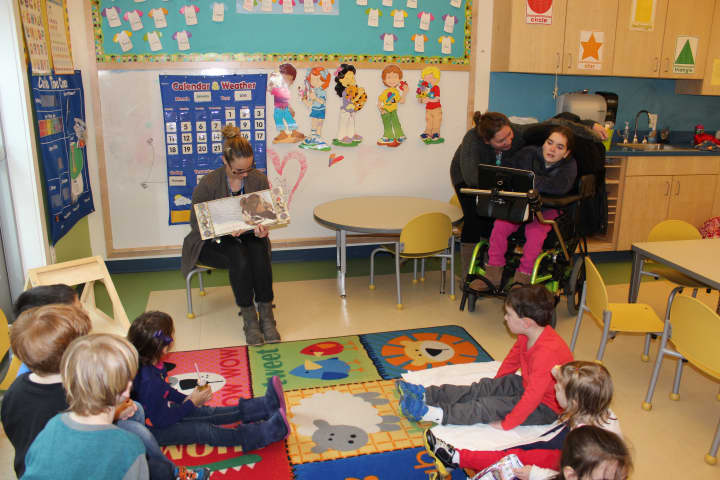 Lauren Stevens, far right, reads to Holly Pond students using her Tobii Communication Device. Aide Piper Garner, second from right, looks on and teacher Brittany Wainacht holds the book. 