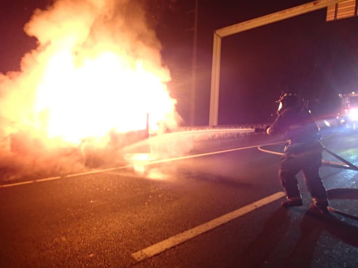 A Westport firefighter attacks the burning car in the breakdown lane of I-95 on Sunday. 