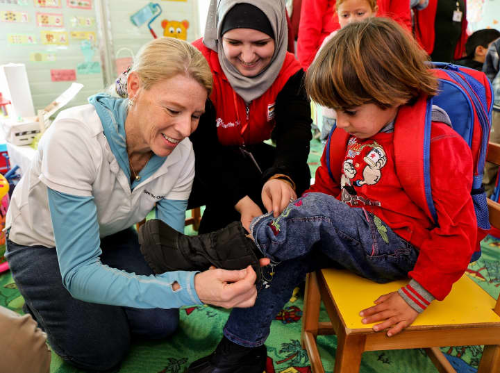 Carolyn Miles, President and CEO of Save the Children, helps a child in one of Save the Childrens child-friendly spaces at the Zaatari refugee camp in Jordan put on a new pair of boots donated by TOMS. 