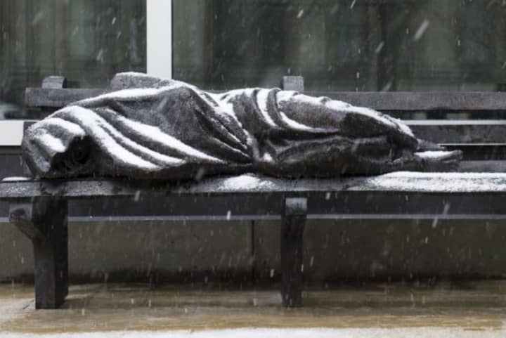 The bronze sculpture depicts Jesus shrouded in a blanket on a bench. 