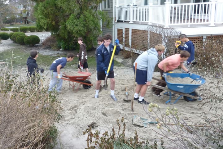 Staples High School soccer players work to remove sand from the front yard of teammate Sebo Hood&#x27;s home on Soundview Drive near Compo Beach in Westport on Wednesday afternoon.