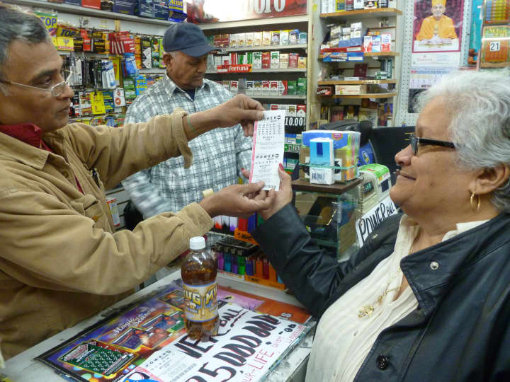 K&#x27;s Cards clerk Pocky Rana hands Powerball tickets to customer Maria Zapata.