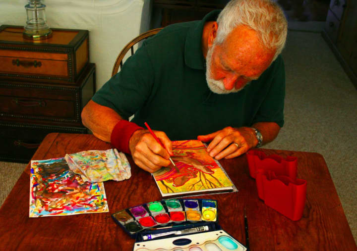 John Newcomb uses a travel kit to create vibrant watercolors on display at Wilton Library in his Travels with John art exhibition.