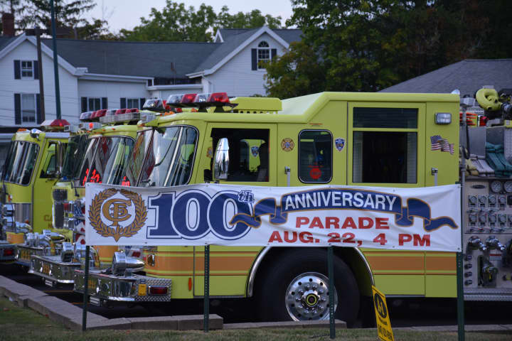 Carmel firetrucks are lined up outside of the firehouse, with a banner announcing the 100th-anniversary parade in front.