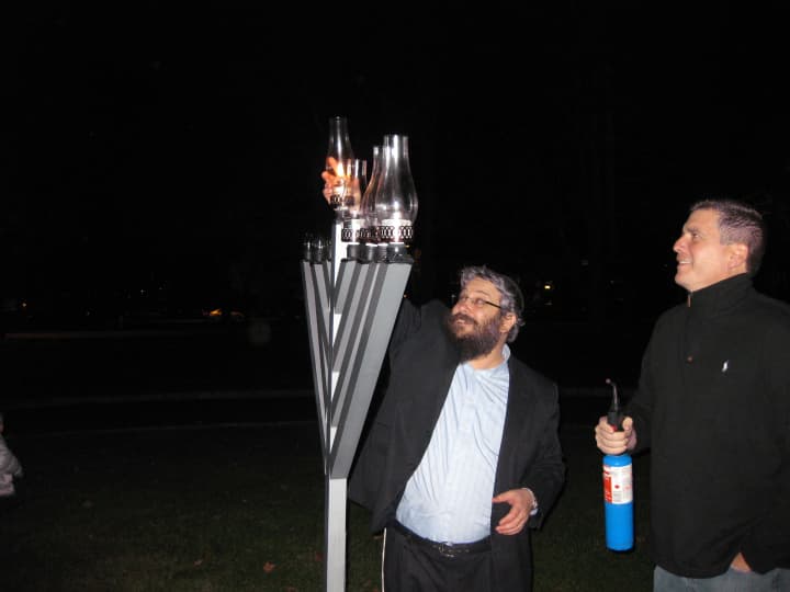 Rabbi Yosef Butman, left, of the Chabad of Armonk lights the first candle on a giant menorah Tuesday outside 99 Business Park Drive.