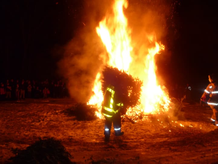 A firefighter feeds a tree into the bonfire with Weston residents watching.