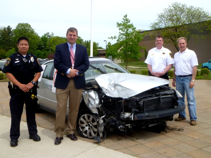 (From Left): School Resource Officer Jason Kim, Principal Bryan Luizzi, Capt. Leon Krolikowski, and Anthony Ceraso, owner of AC Auto Body, outside New Canaan High School with a damaged car reminding students not to drink and drive. 