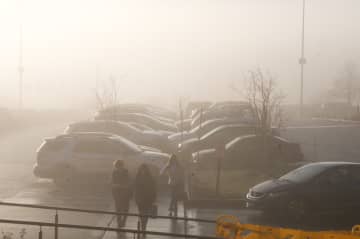 Shoppers navigate a foggy parking lot as fog, rain and warm temperatures envelop the area.