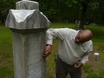 David Thomas scrapes off linchen, a fungus, off a grave stone as part of the effort to restore the African-American Cemetery in Rye. 