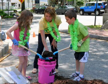Terry Pike, co-chair of the Partnership's Pound Ridge Pride Day, helps two youngsters do some planting in Scotts Corner.
